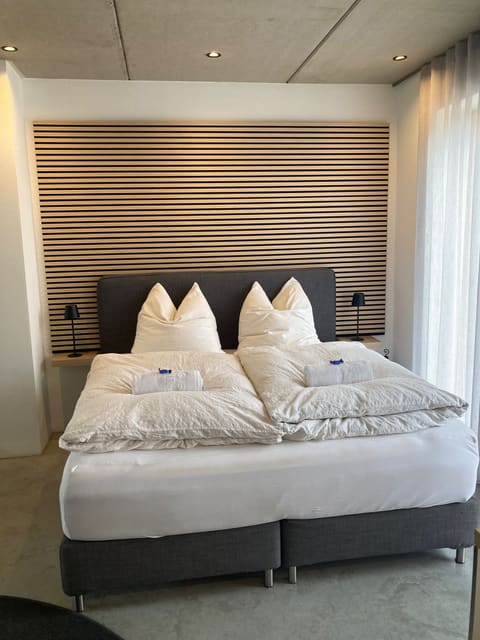 Studio im Grünen: Boxspringbett vor einer Holzlamellenwand, helles Fenster